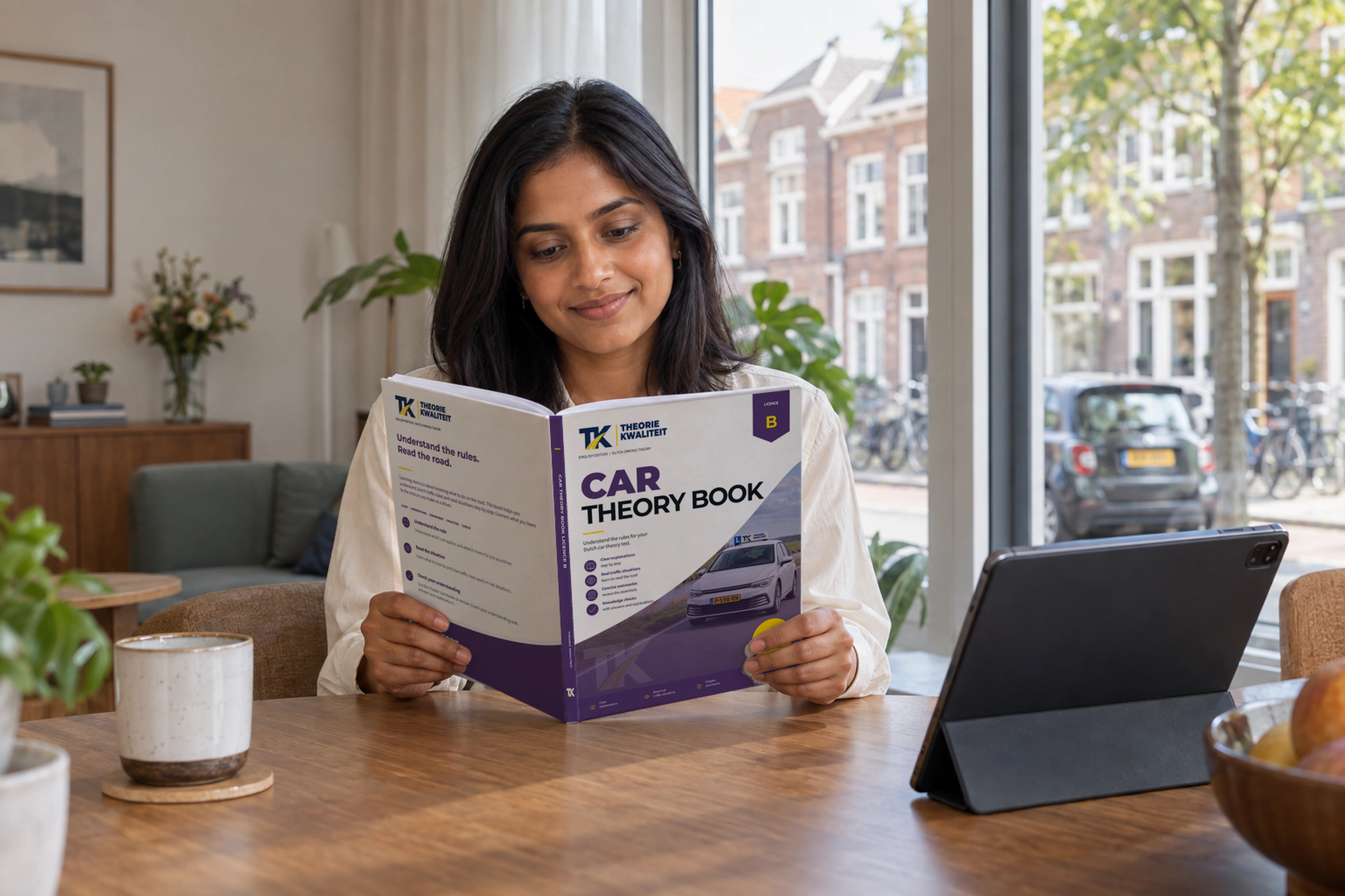 Learner reads the English Edition Car Theory Book beside a tablet.